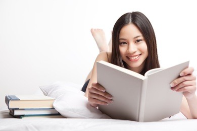a shot of a beautiful asian college student reading on her bed