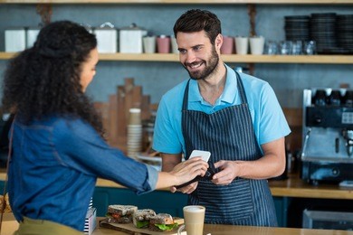 woman paying bill through smartphone using nfc technology in cafe