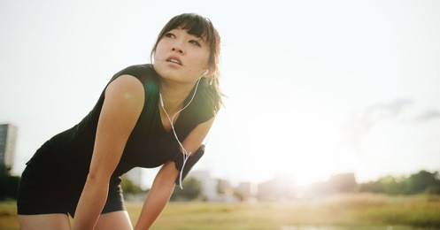 young athletic woman taking a break from training. chinese female standing with hands on her knees and looking away in morning.