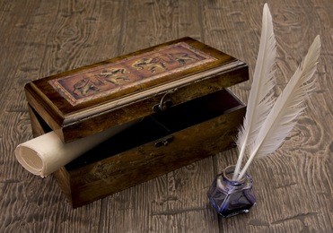 the ancient chest with a paper inside stands on a table near to a feather and ink