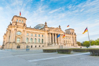 german reichstag, the german parliament building in berlin at sunset. some german flags and one european waving. politics and architecture concepts.