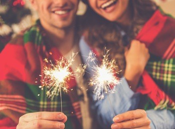 cropped image of happy young couple holding sparklers, hugging and smiling while celebrating christmas at home