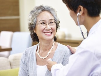 family doctor checking smiling senior asian woman using stethoscope