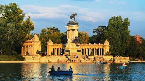 madrid, spain. people inside vessel boats in the pond of buen retiro park with monument to alfonso xii and blue sky at the background. sunny day in the evening in madrid