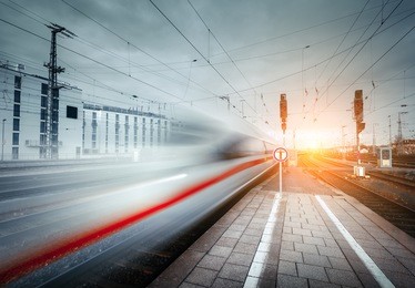 high speed passenger train on railroad track in motion at sunset. blurred commuter train. railway platform in the city. railway station in europe. railroad with vintage toning. industrial landscape