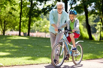 family, generation, safety and people concept - happy grandfather teaching boy how to ride bicycle at summer park