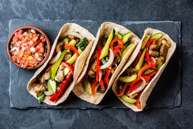 mexican pork tacos with vegetables and salsa. tacos al pastor on black stone slate plate on black background. top view