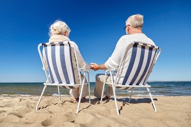 family, old age, travel, tourism and people concept - happy senior couple sitting on deck chairs on summer beach