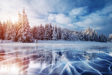 cracks on the surface of the blue ice. frozen lake in winter mountains. it is snowing. the hills of pines. carpathian ukraine europe.