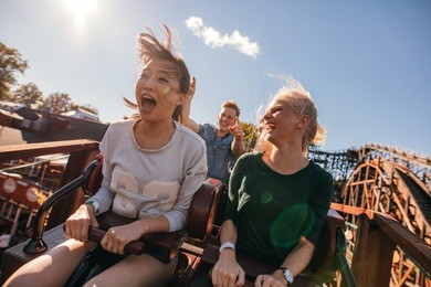 young friends on thrilling roller coaster ride. young women and men having fun at amusement park.