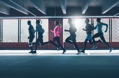 group of diverse urban runners sprinting across the frame in an indoor car park as they workout backlit by the sun through a grid