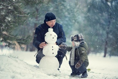 cute little boy in earflaps hat with his father are making a snowman. image with selective focus and toning