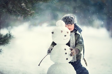 cute little boy in earflaps hat with a snowman. image with selective focus and toning