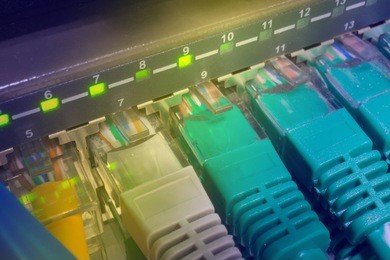 close up of green and blue network cables connected to black switch patch panel glowing in the dark. gradient toned