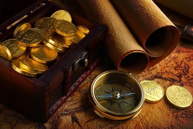 old brass compass lying on a very old map with treasure chest full of golden coins