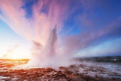 strokkur geyser eruption in iceland. fantastic colors shine through the steam. beautiful pink clouds in a blue sky.