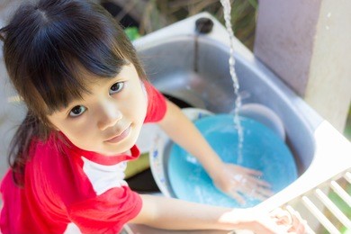 asian girl help parents work , she wash the dish happily.