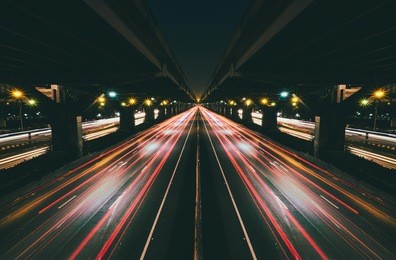 fast moving traffic with red light trails on black asphalt motorway and tollway on above at night. shot with long time exposure and mirror effect.