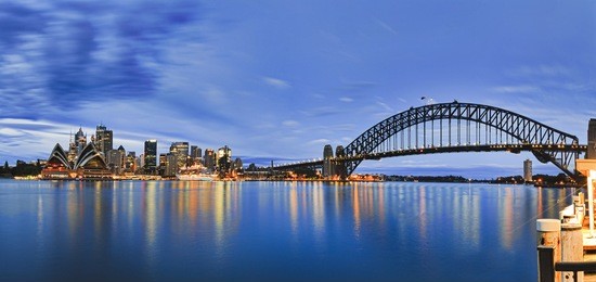 landmarks of sydney city cbd across harbour with bridge, circular quay, passenger terminal and downtown skyscrapers to kirribilli pier at blue cloudy sunrise.