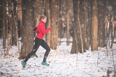 winter running exercise. runner jogging in snow. young woman fitness model running in a city park 