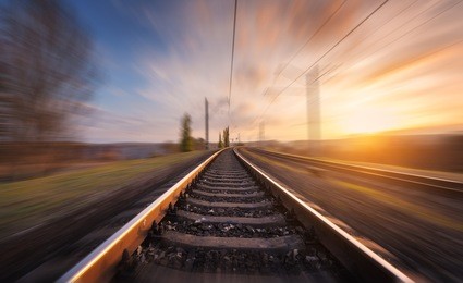 railroad in motion at sunset. railway station with motion blur effect against beautiful blue sky, industrial concept background. railroad travel, railway tourism. blurred railway. transportation