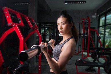 beautiful asian woman is doing exercises with the bar in the gym, sporty woman exercising with barbell in gym, bodybuilding and people concept.