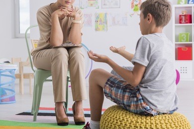 child sitting on a pouf, talking with a psychologist