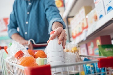 man doing grocery shopping at the supermarket, he is putting a bottle of milk in the cart
