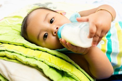 asian baby infant eating milk from bottle, 9 months after birth