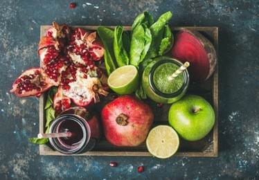 green and purple fresh juices or smoothies with fruit, greens, vegetables in wooden tray, top view, selective focus. detox, dieting, clean eating, vegetarian, vegan, fitness, healthy lifestyle concept