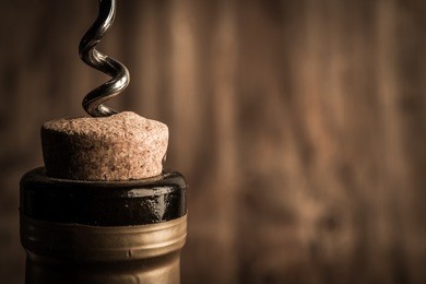 bottle of wine with corkscrew on wooden background