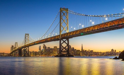 classic panoramic view of famous oakland bay bridge with the skyline of san francisco in the background illuminated in beautiful twilight after sunset in summer, california, usa