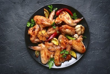 grilled chicken wings on a black plate on a stone,concrete or slate background.top view.