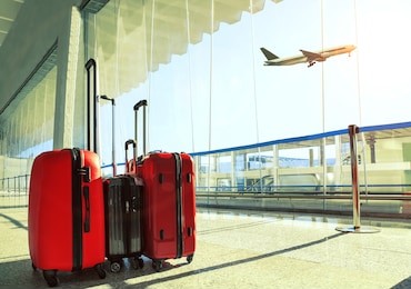 stack of traveling luggage in airport terminal and passenger plane flying over sky
