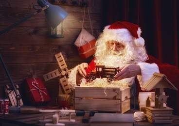 merry christmas and happy holidays! santa claus is preparing gifts for children for xmas at his desk at home. christmas legends and traditions.
