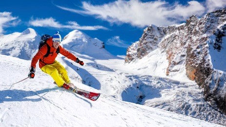 skier skiing downhill in high mountains against sunshine