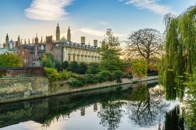 view of cam river and the ornamented facade of clare college at sunrise in cambridge, uk