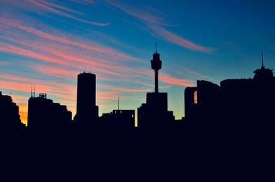 sunrise in sydney with sydney tower and skyscrapers in silhouette.