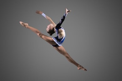 gymnast girl doing splits in the air. beautiful cool young fit gymnast woman in blue sportswear dress working out, performing art gymnastics element, jumping, doing split leap in the air, dancing