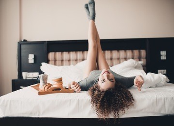 beautiful smiling girl 20-24 year old having fun in bed with breakfast on wooden tray. wearing knitted socks and t-shirt. looking at camera. 