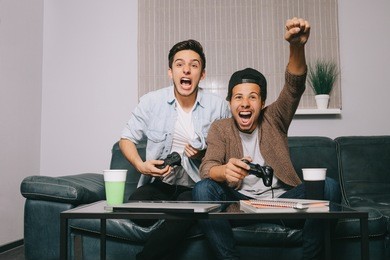 two guys playing on the console sitting on the couch. european and african friends had a party. victory celebration