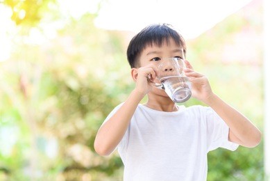 young thai boy drinking water from glass in the garden
