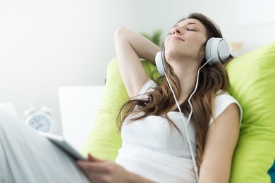 beautiful young woman with headphones relaxing on the bed, she is listening to music using a tablet, chill out and leisure concept 