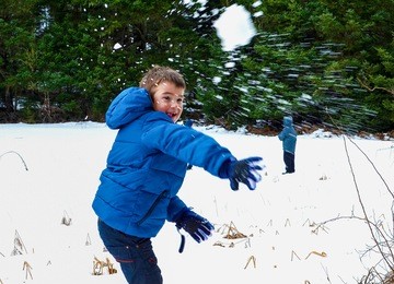 boy in blue warm coat having fun in beautiful winter place with snowballs