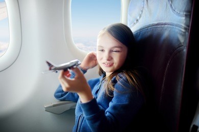 adorable little girl traveling by an airplane. child sitting by aircraft window and playing with toy plane. 