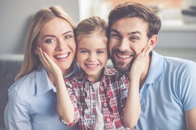 portrait of beautiful young parents and their cute little daughter hugging, looking at camera and smiling