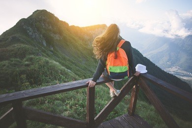 young traveling woman with backpack sitting high on the top of the mountain with waving hair, evening with sunset