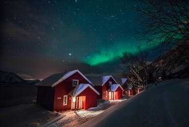 northern lights (aurora borealis) over the red snowed-in cottages in lapland village