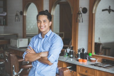 confident barber expert. young man looking at camera and smiling standing at barbershop