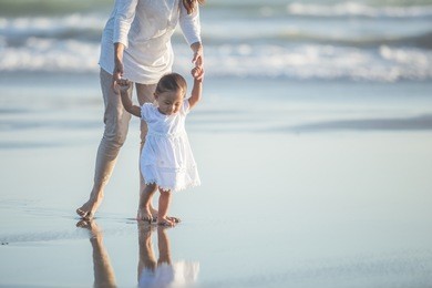 portrait of a mother is teaching her daughter walks on the beach